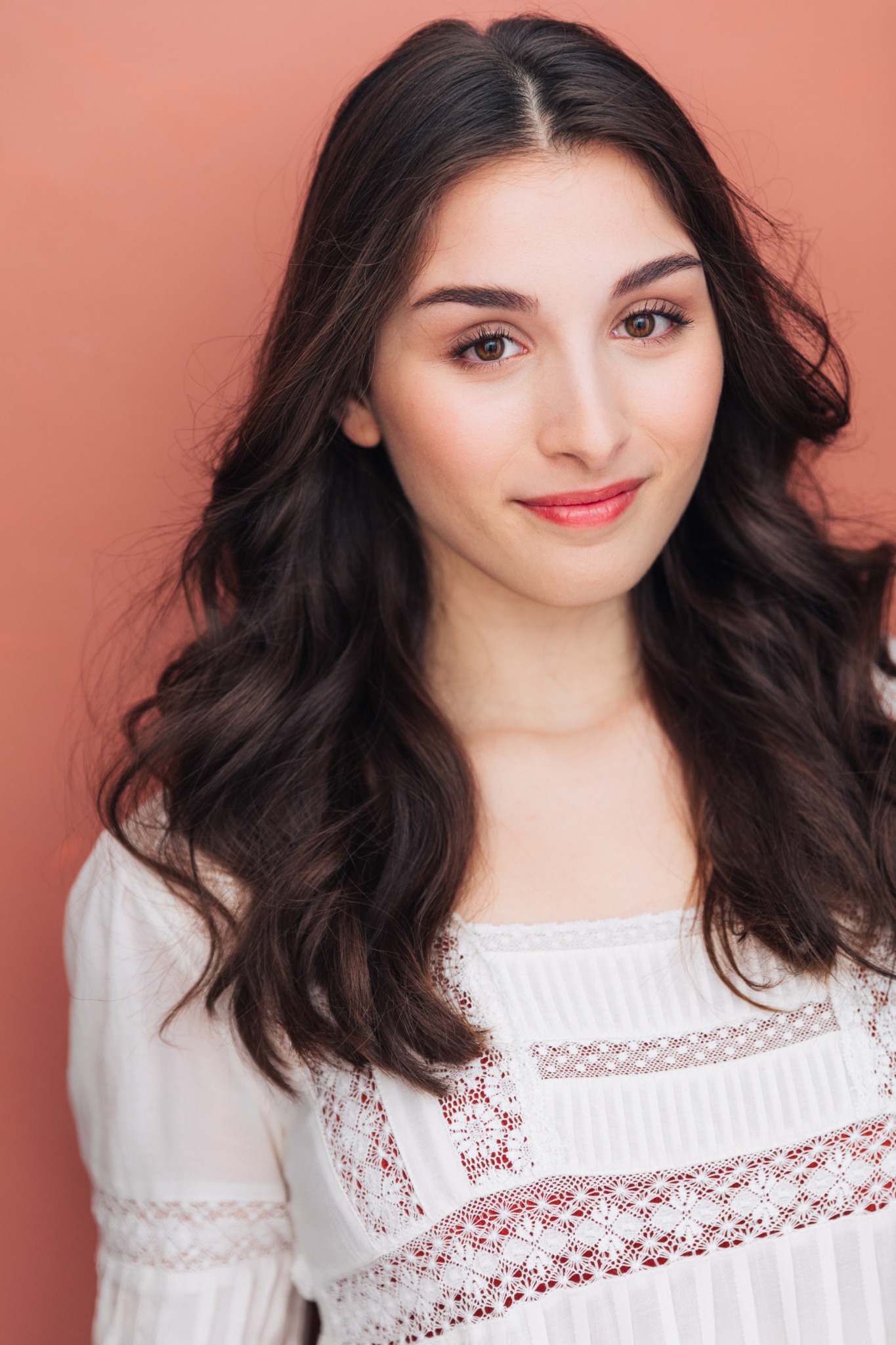 Portrait of Annabelle Kempf in a white blouse against a warm coral background